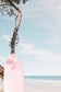 a pink surfboard leaning against a tree on the beach